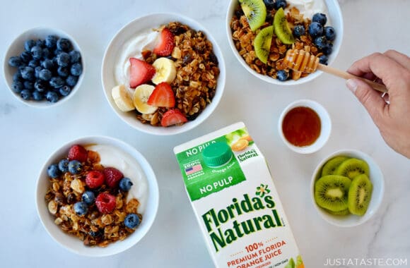 A top-down view of granola parfaits in bowls and a carton of orange juice