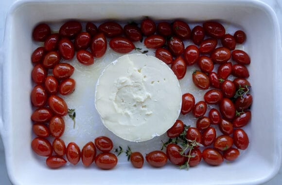 A wheel of Brie cheese surrounded by cherry tomatoes