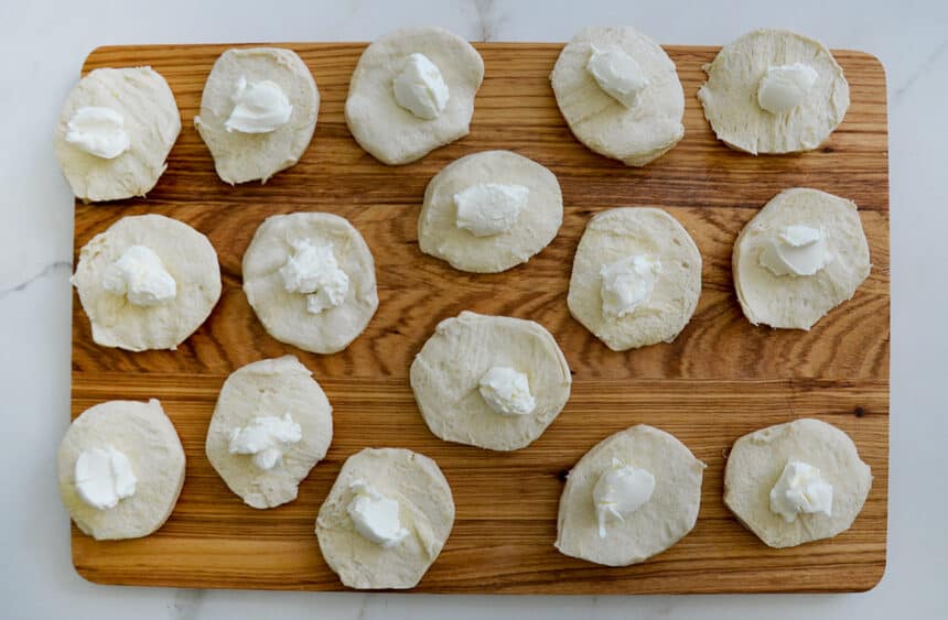 Top-down view of a wood cutting board with biscuits containing a dollop of cream cheese