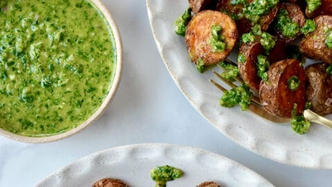 A top-down view of two white plates containing roasted potatoes topped with chimichurri sauce