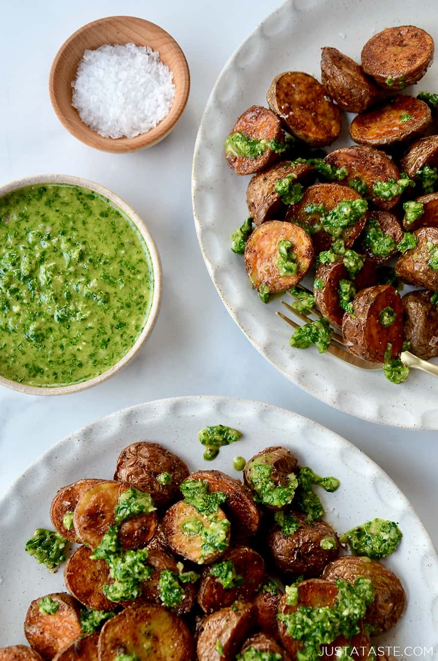A top-down view of two white plates containing roasted potatoes topped with chimichurri sauce
