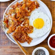 Image for Pinterest that shows homemade crispy hash browns on a white plate with fork and a fried egg next to small ramekins containing pepper and ketchup.
