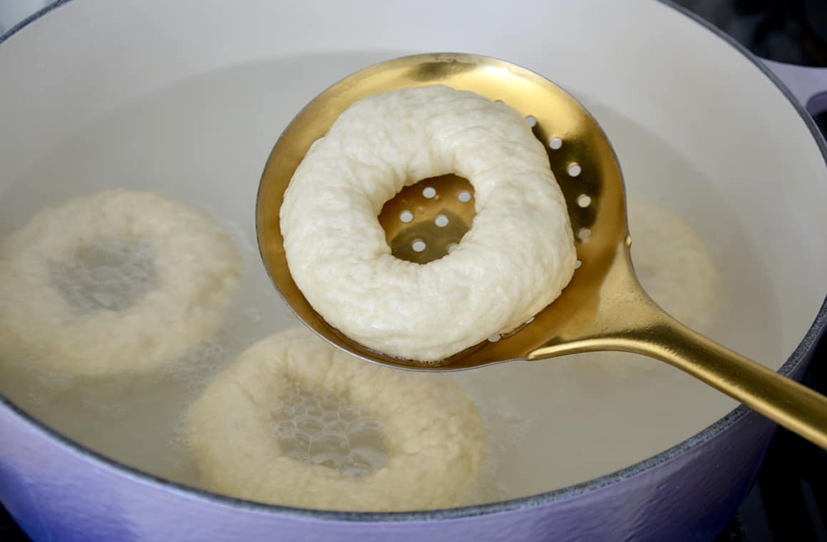 A soft pretzel bagel being dipped in a baking soda bath