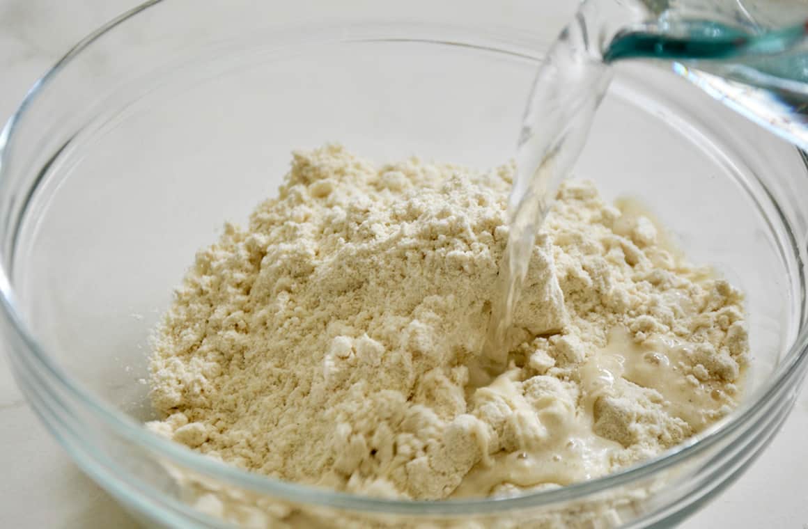 Masa harina in a glass bowl with water being poured in