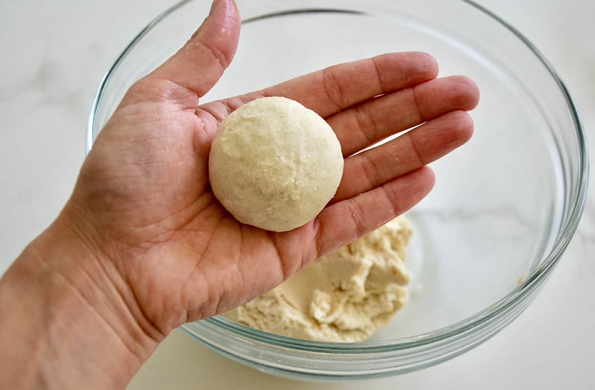 A hand holding corn tortilla dough shaped into a ball