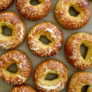Top-down view of Easy Soft Pretzel Bagels topped with large-flake sea salt above grey writing that says, "Soft Pretzel Bagels" and the purple Just a Taste logo.
