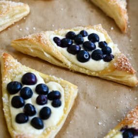 Blueberry cream cheese puff pastries dusted with sanding sugar on brown parchment paper.