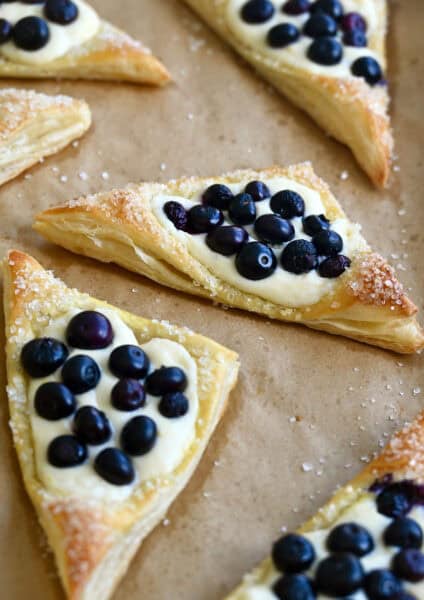 Blueberry cream cheese puff pastries dusted with sanding sugar on brown parchment paper.