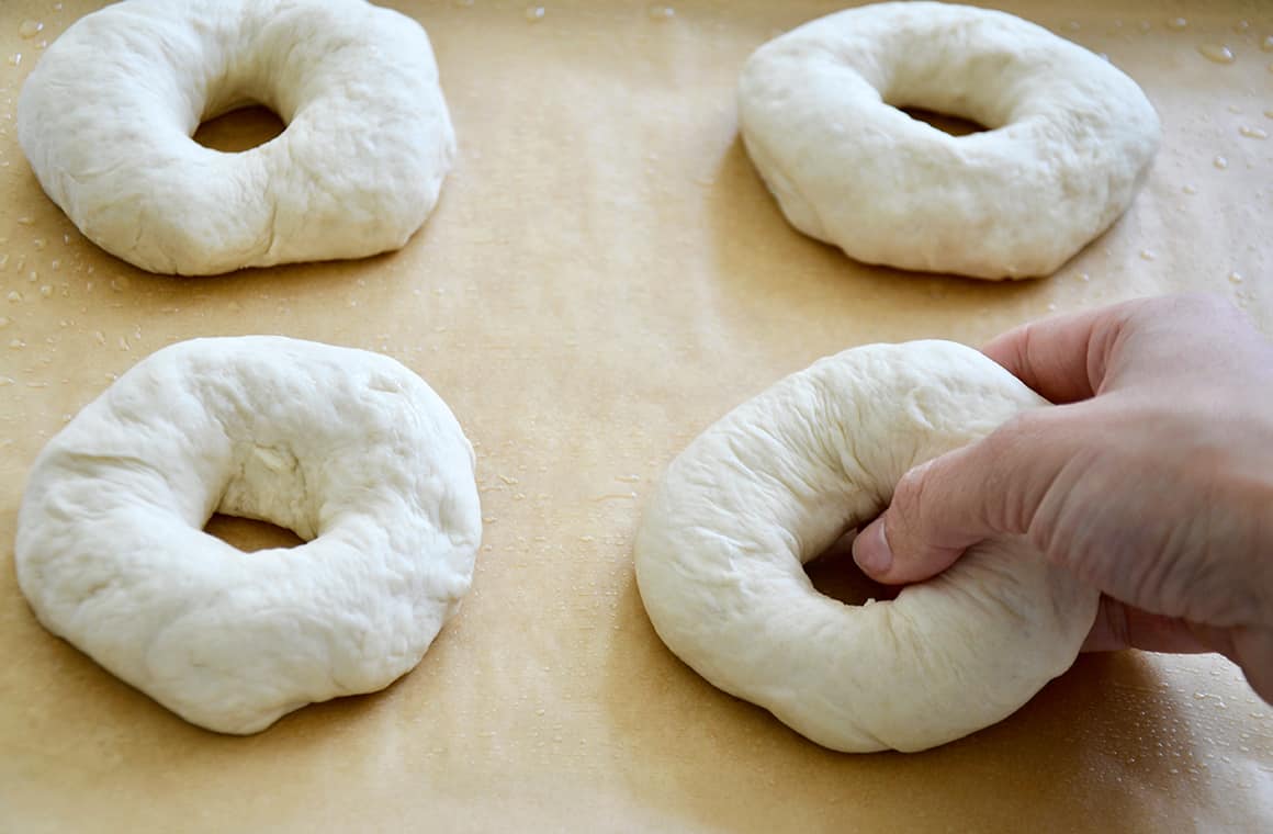 A hand shaping soft pretzel bagels on a baking sheet