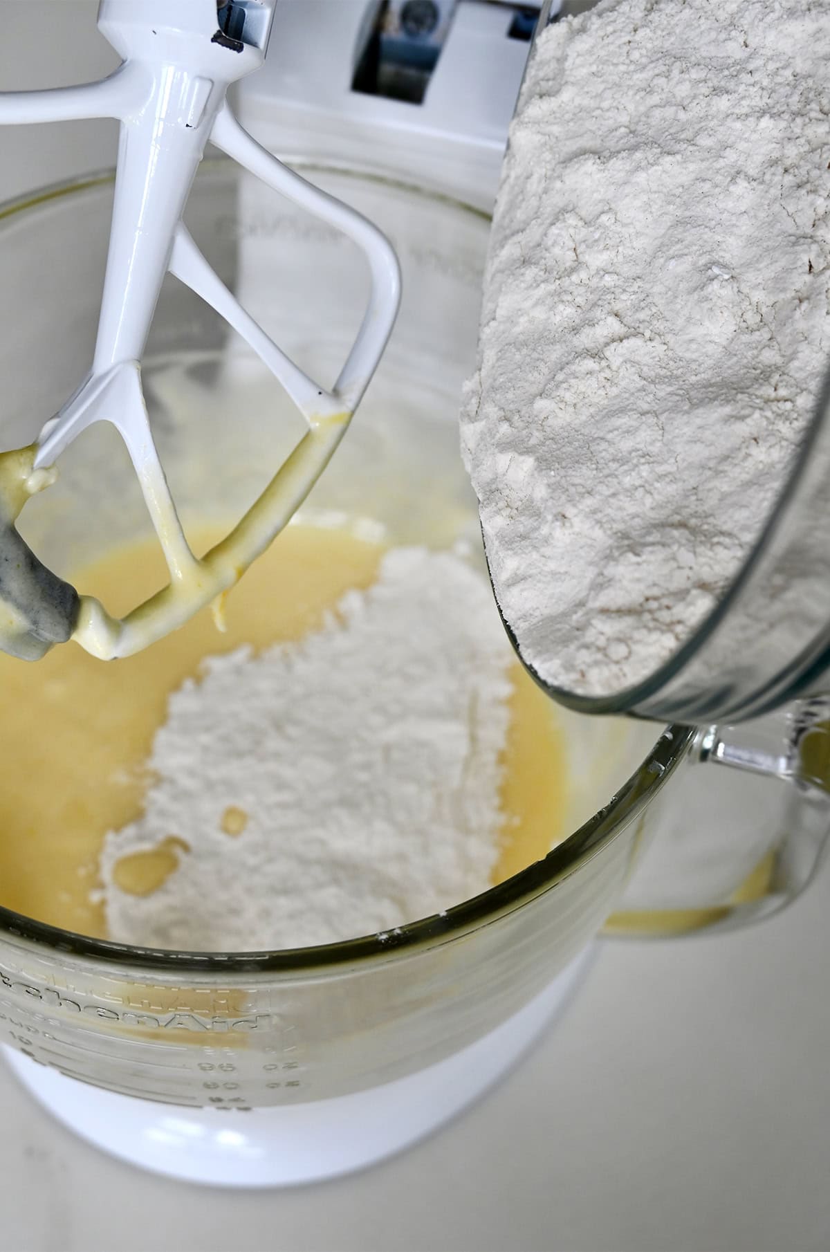 Adding dry ingredients to wet ingredients in a stand mixer bowl to make a sour cream muffin batter.