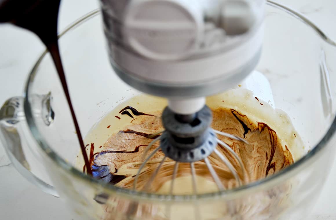 A stand mixer with the whisk attachment and chocolate being poured in