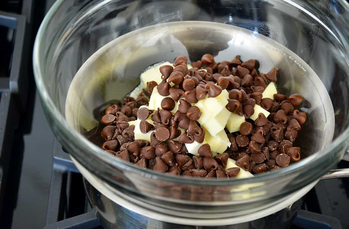 A glass bowl filled with chocolate chips and butter set above a double-boiler