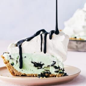 Mint chocolate chip ice cream pie with a waffle cone crust topped with a thick layer of whipped cream and drizzled with chocolate syrup.