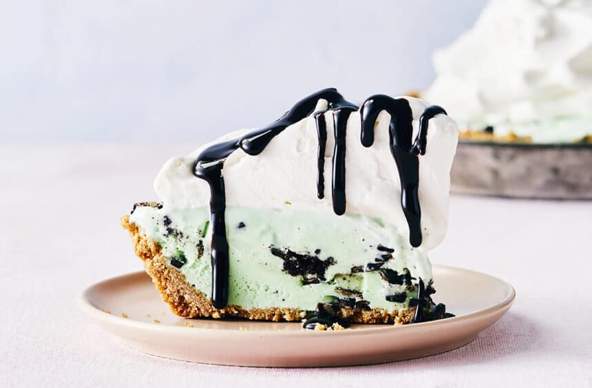 A slice of ice cream pie on a pink plate with whipped cream and chocolate sauce