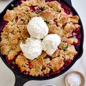 A cast-iron skillet with fruit crumble topped with ice cream