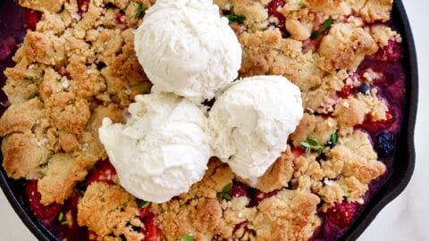 A cast-iron skillet with fruit crumble topped with ice cream