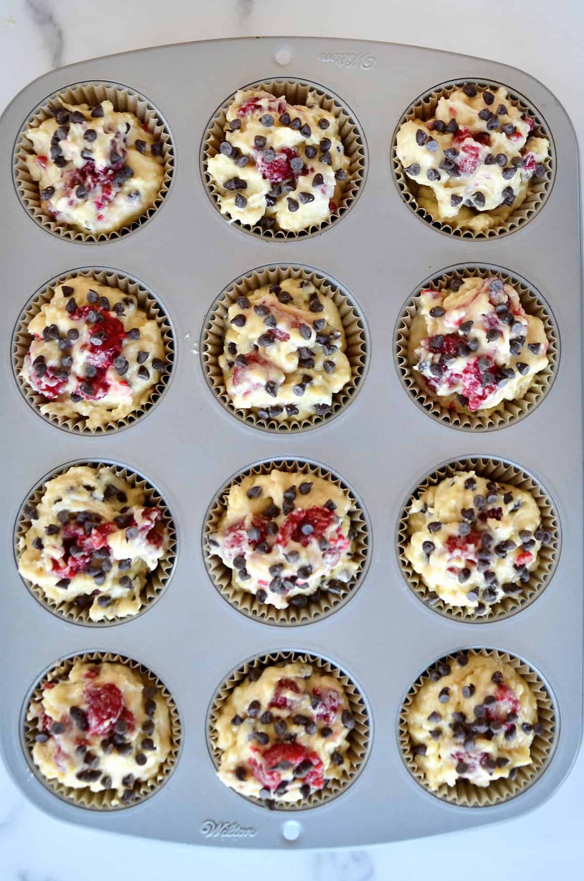 Raspberry muffin batter studded with mini chocolate chips in a lined muffin pan.