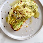 Top-down view of a Pesto Egg atop toasted bread with avocado garnished with crushed red pepper flakes and grated parmesan cheese.