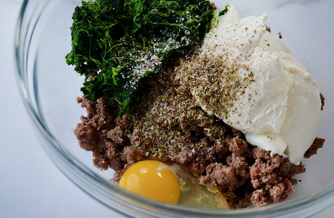 A glass bowl containing ground beef, ricotta, spinach and eggs