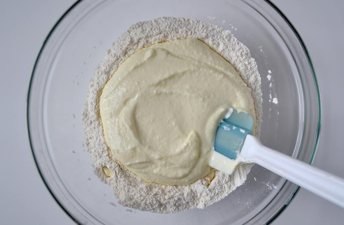 A glass bowl containing yogurt pancake batter and a spatula