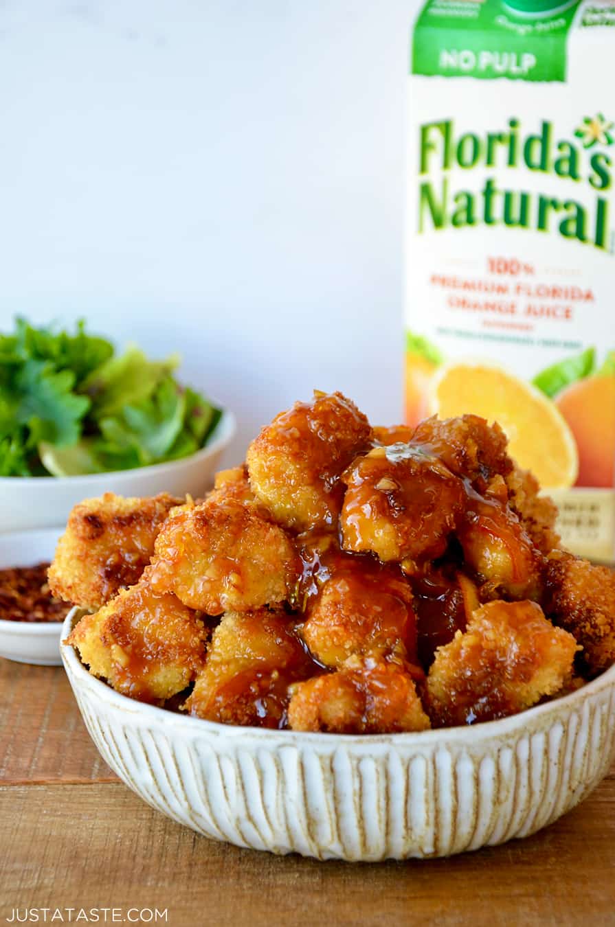 A white bowl containing baked orange chicken with a carton of Florida's Natural Orange Juice in the background