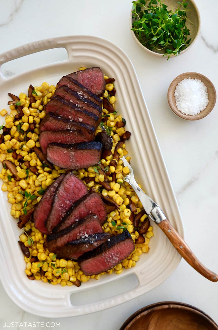 A white platter containing steak and corn with thyme