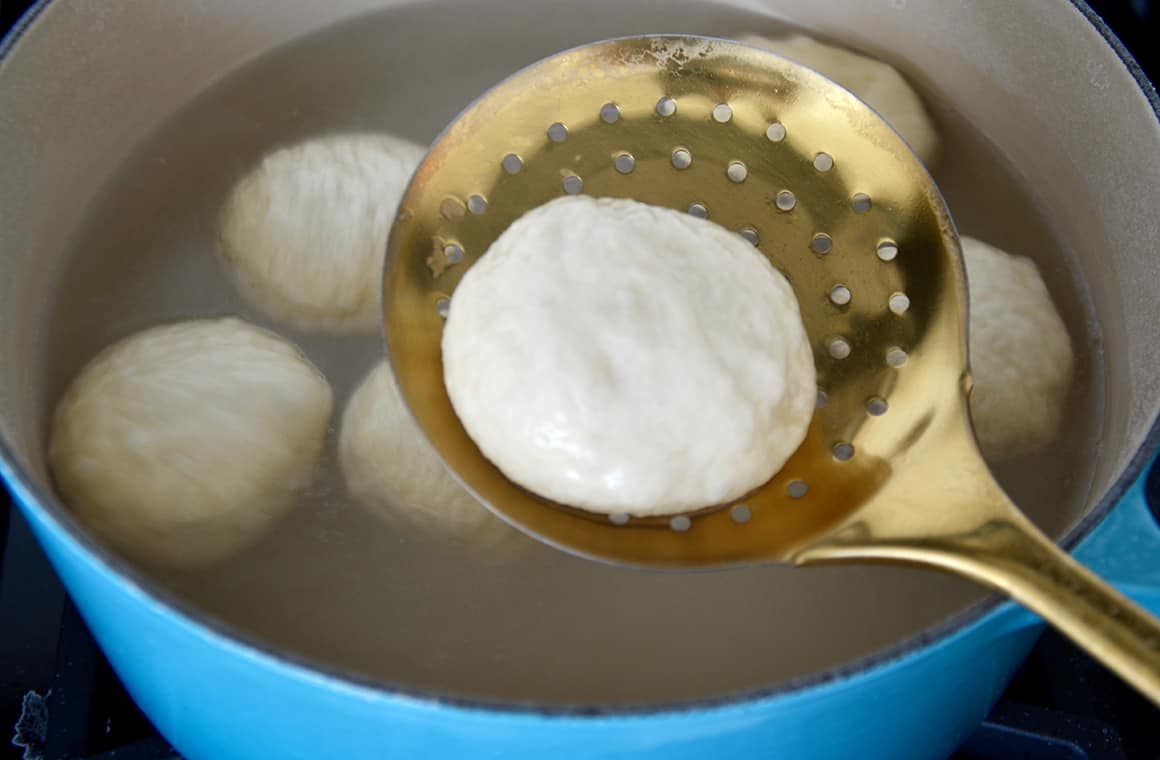 A ball of soft pretzel dough being dipped into a baking soda bath
