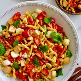 A large white bowl containing pasta salad with small wood plates next to it