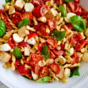 A large white bowl containing pasta salad with chicken, mini mozzarella balls, cherry tomatoes and fresh basil.