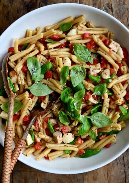 A top-down view of a large serving bowl containing Caprese pasta salad garnished with fresh basil leaves.