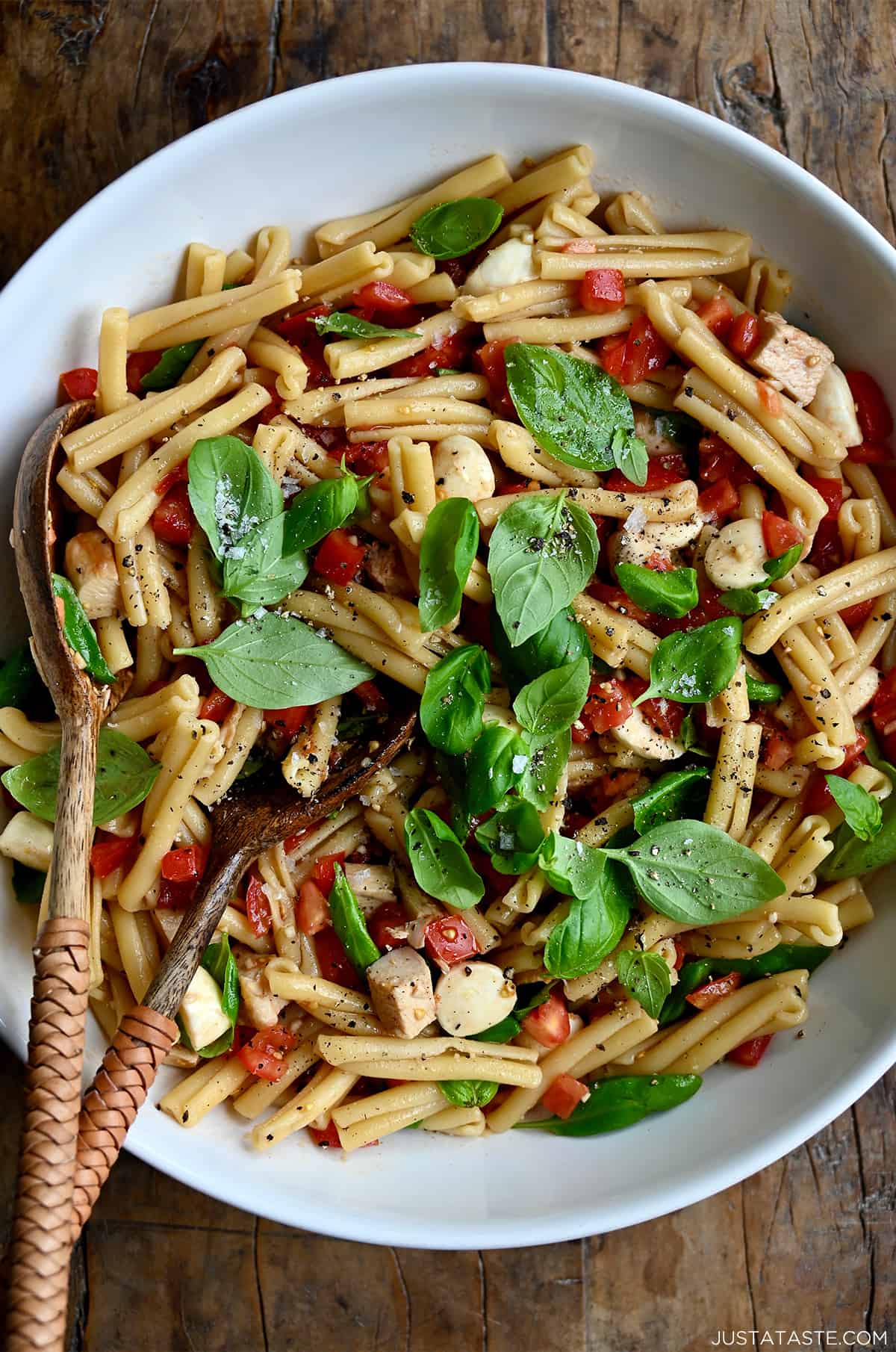 A top-down view of a large serving bowl containing Caprese pasta salad garnished with fresh basil leaves.