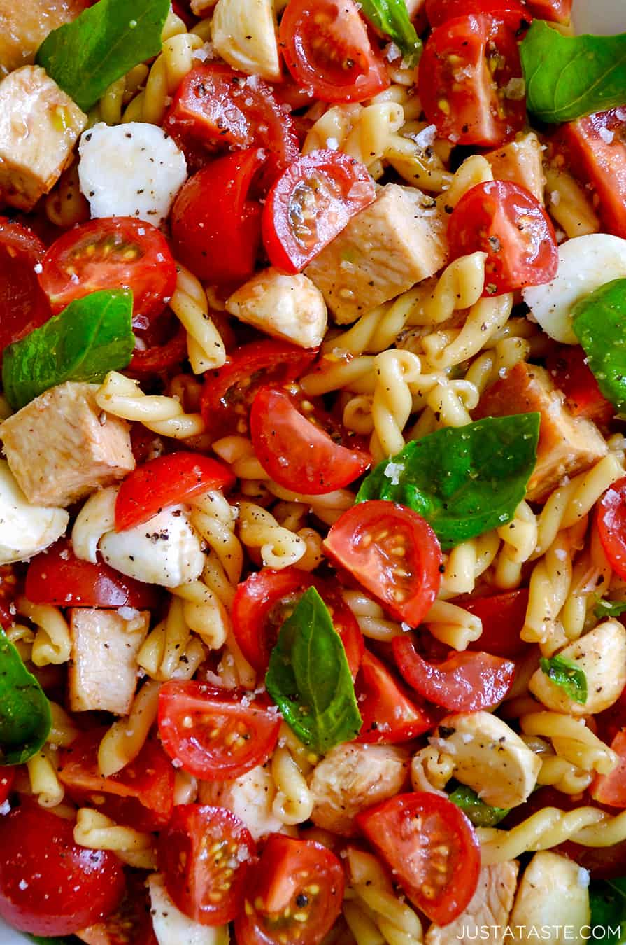 A close-up of pasta, tomatoes, basil, chicken and mozzarella cheese