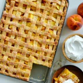 A slab pie surrounded by whipped cream and peaches