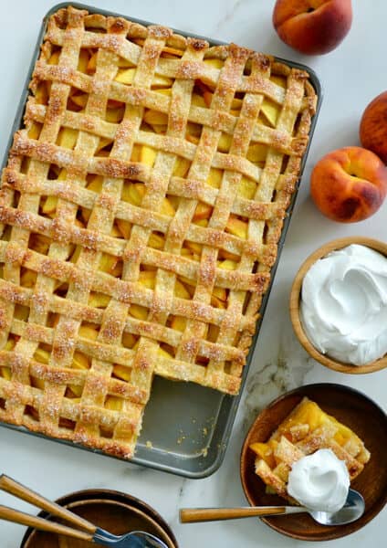 A slab pie surrounded by whipped cream and peaches