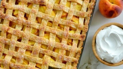 A slab pie surrounded by whipped cream and peaches