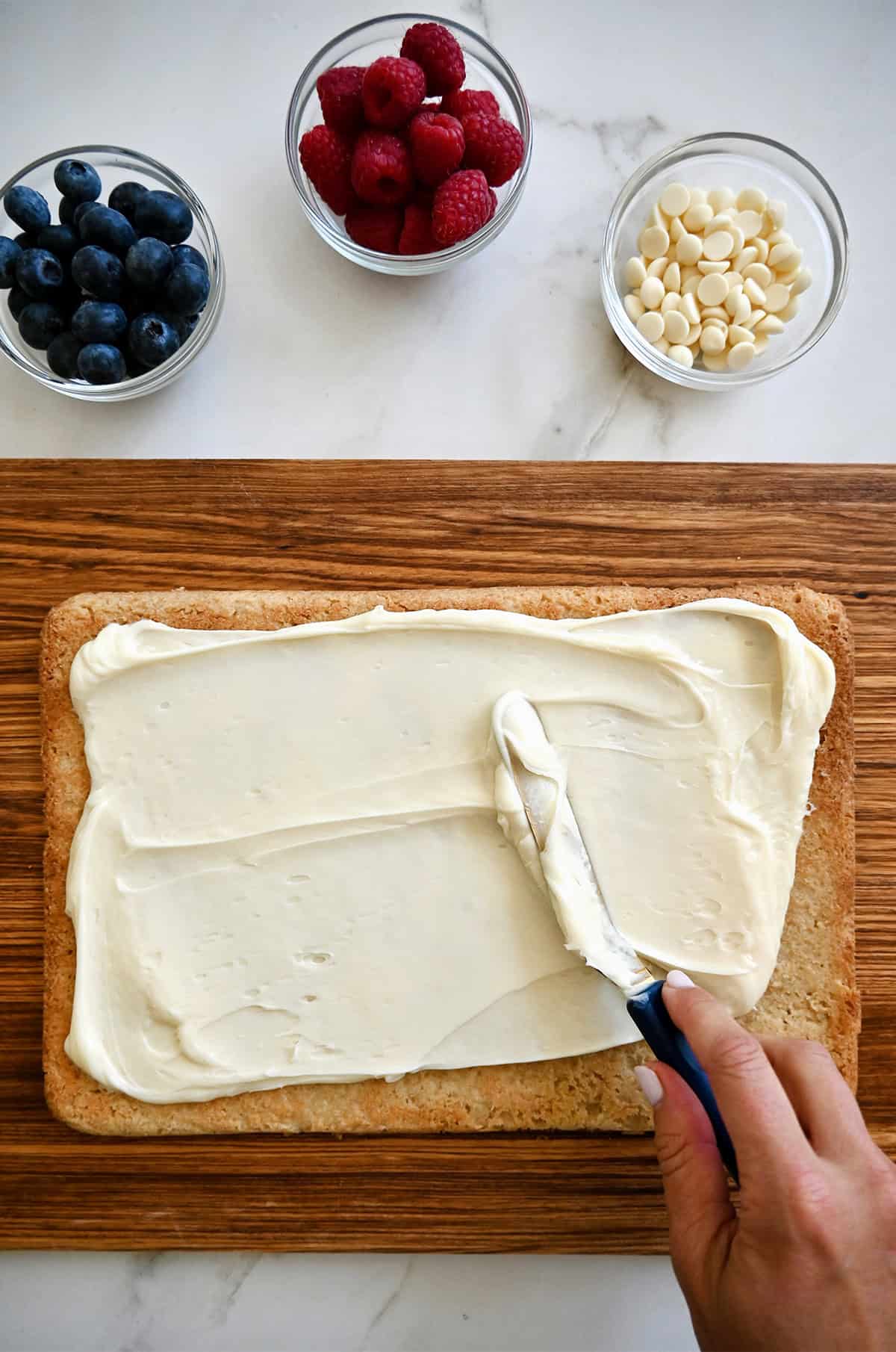 Spreading cream cheese frosting atop a shortbread cookie cake with an offset spatula.
