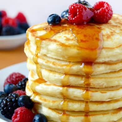 A tall stack of fluffy Greek yogurt pancakes topped with fresh berries and a drizzle of maple syrup.