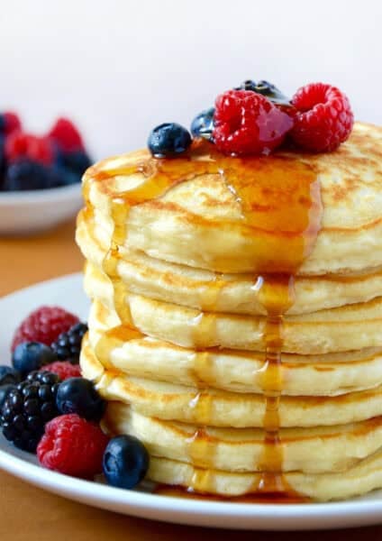 A tall stack of fluffy Greek yogurt pancakes topped with fresh berries and a drizzle of maple syrup.