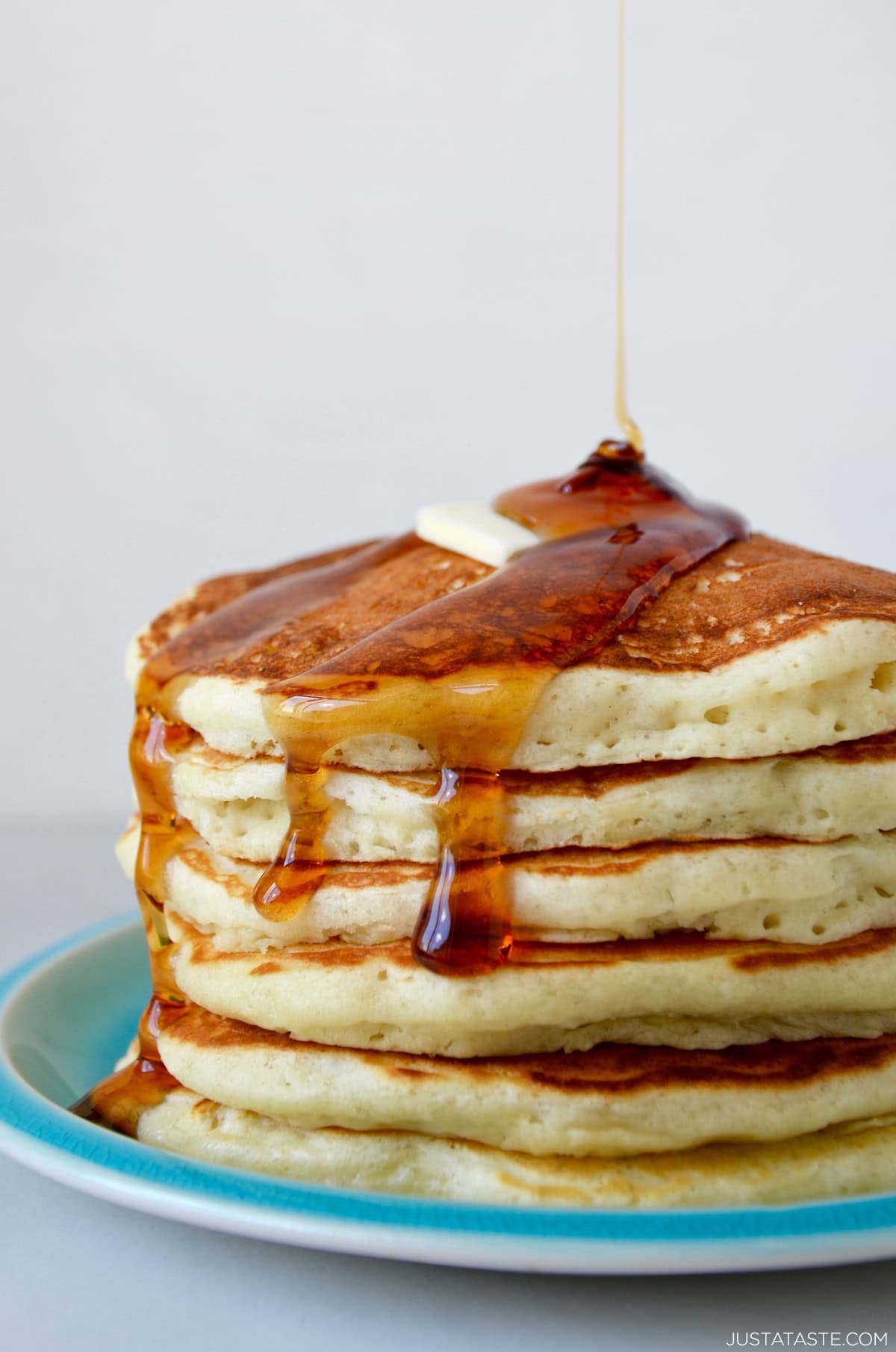 A tall stack of fluffy, protein-packed Greek yogurt pancakes topped with a pad of butter and a thick drizzle of maple syrup.