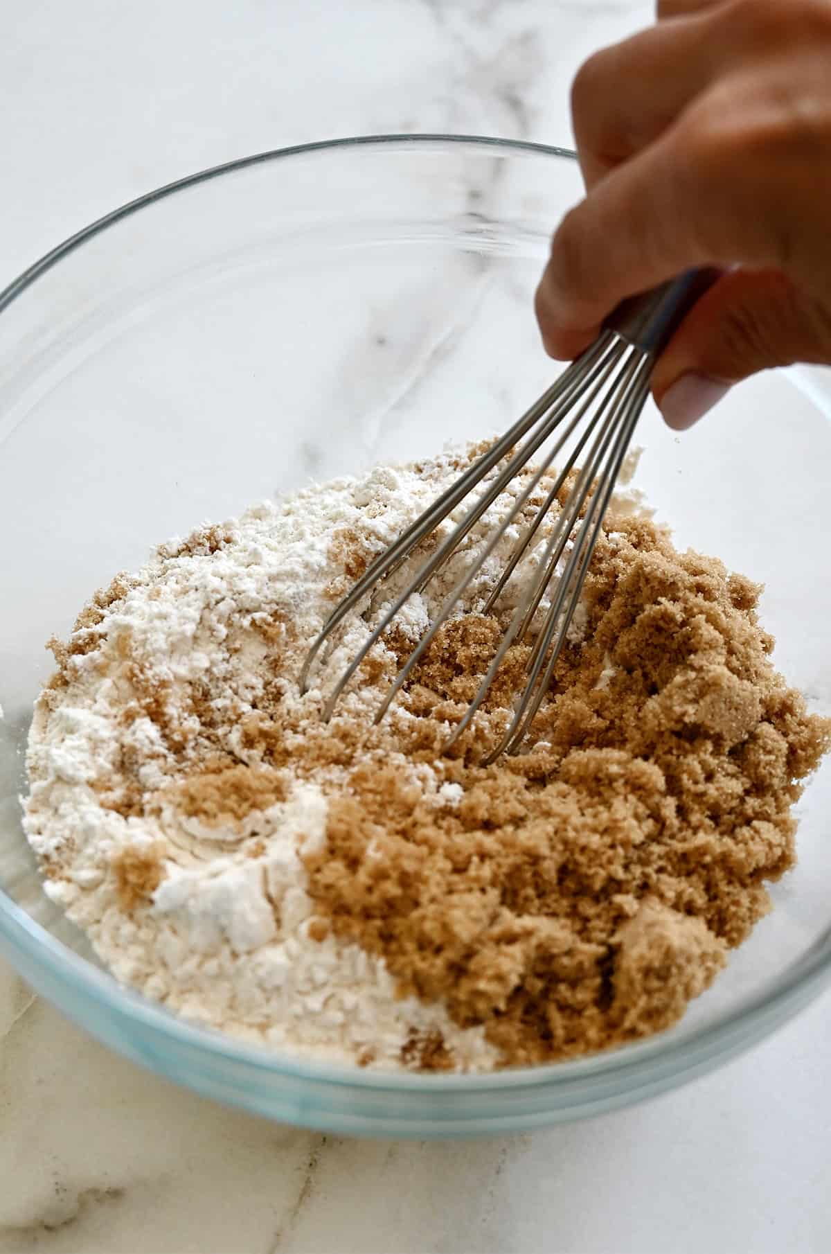 Brown sugar and flour being whisked together in a mixing bowl.