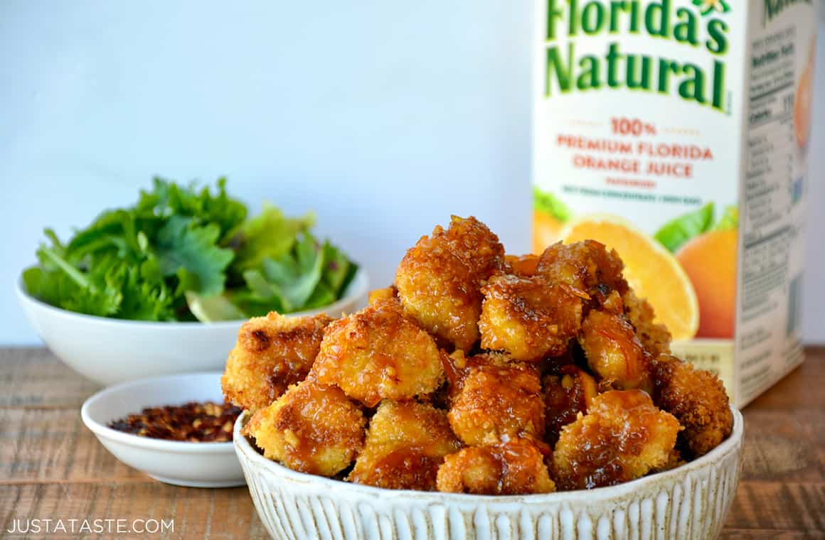 A white bowl containing orange chicken poppers with a carton of orange juice in the background