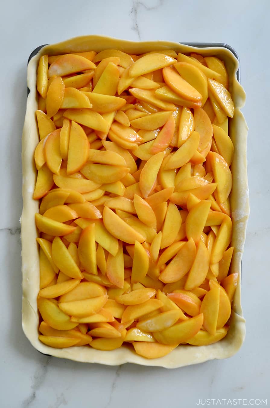 A top-down view of sliced peaches inside a pie crust on a baking sheet