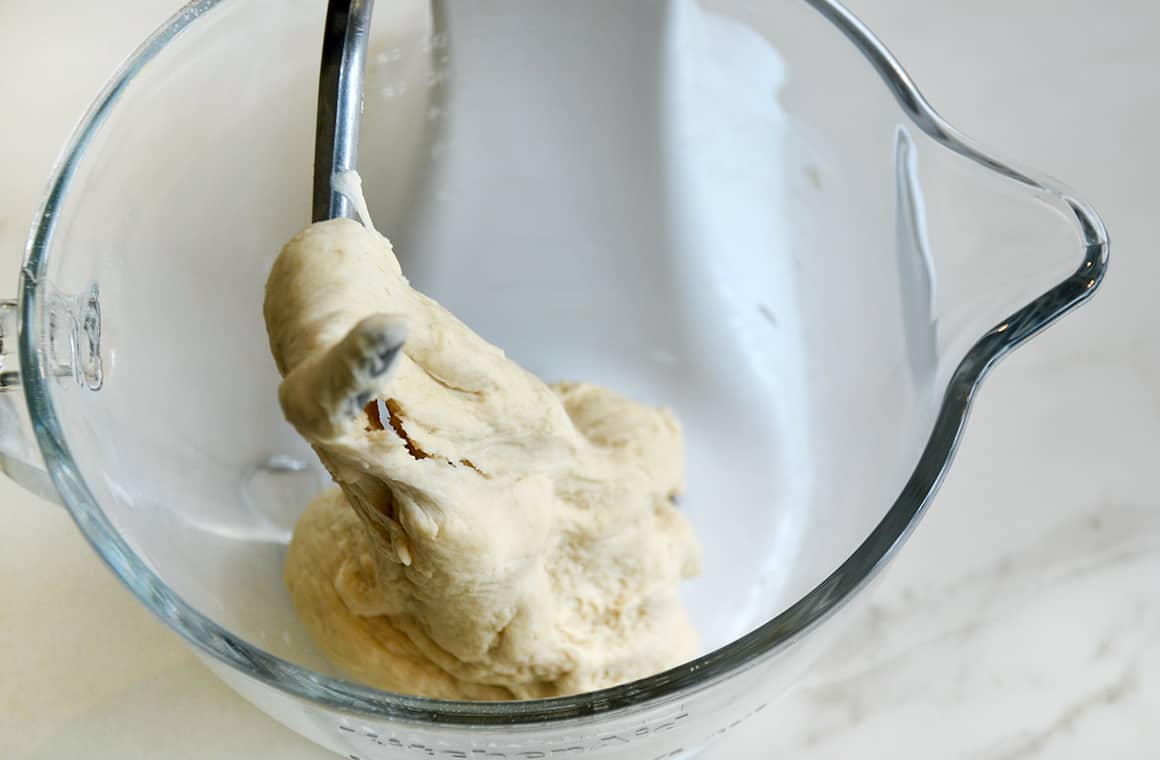 Pretzel dough wrapped around a dough hook in a glass bowl