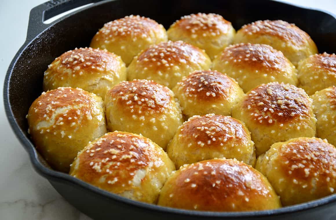 A cast-iron skillet with soft pretzel rolls topped with salt