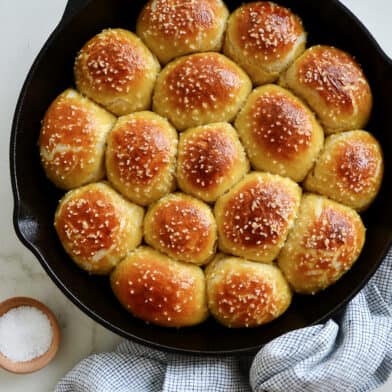 A cast-iron skillet filled with pretzel rolls with a small bowl of salt