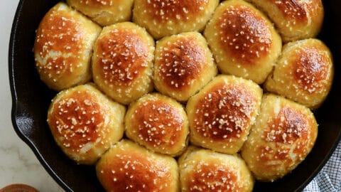 A cast-iron skillet filled with pretzel rolls with a small bowl of salt