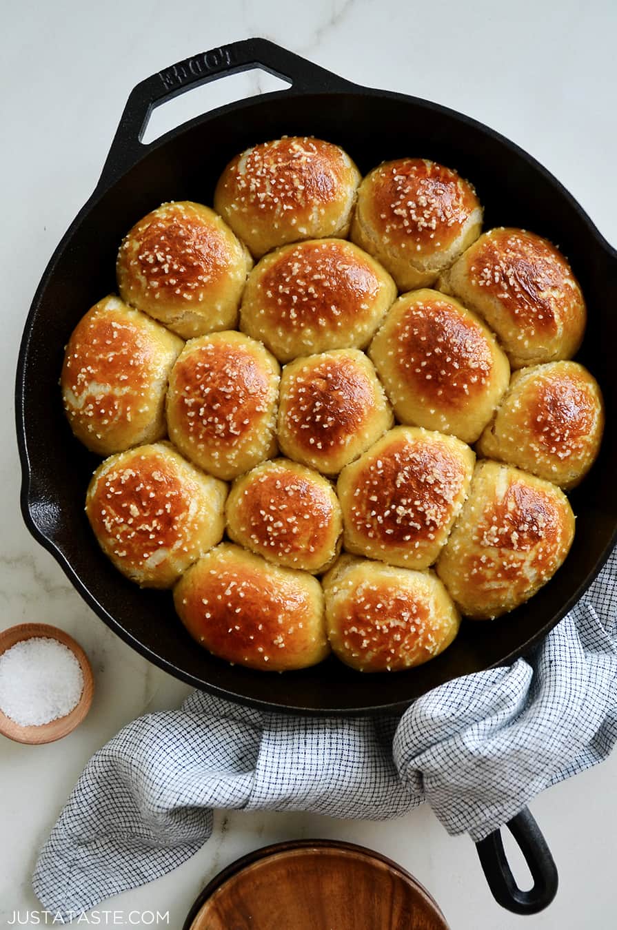 A cast-iron skillet filled with pretzel rolls with a small bowl of salt