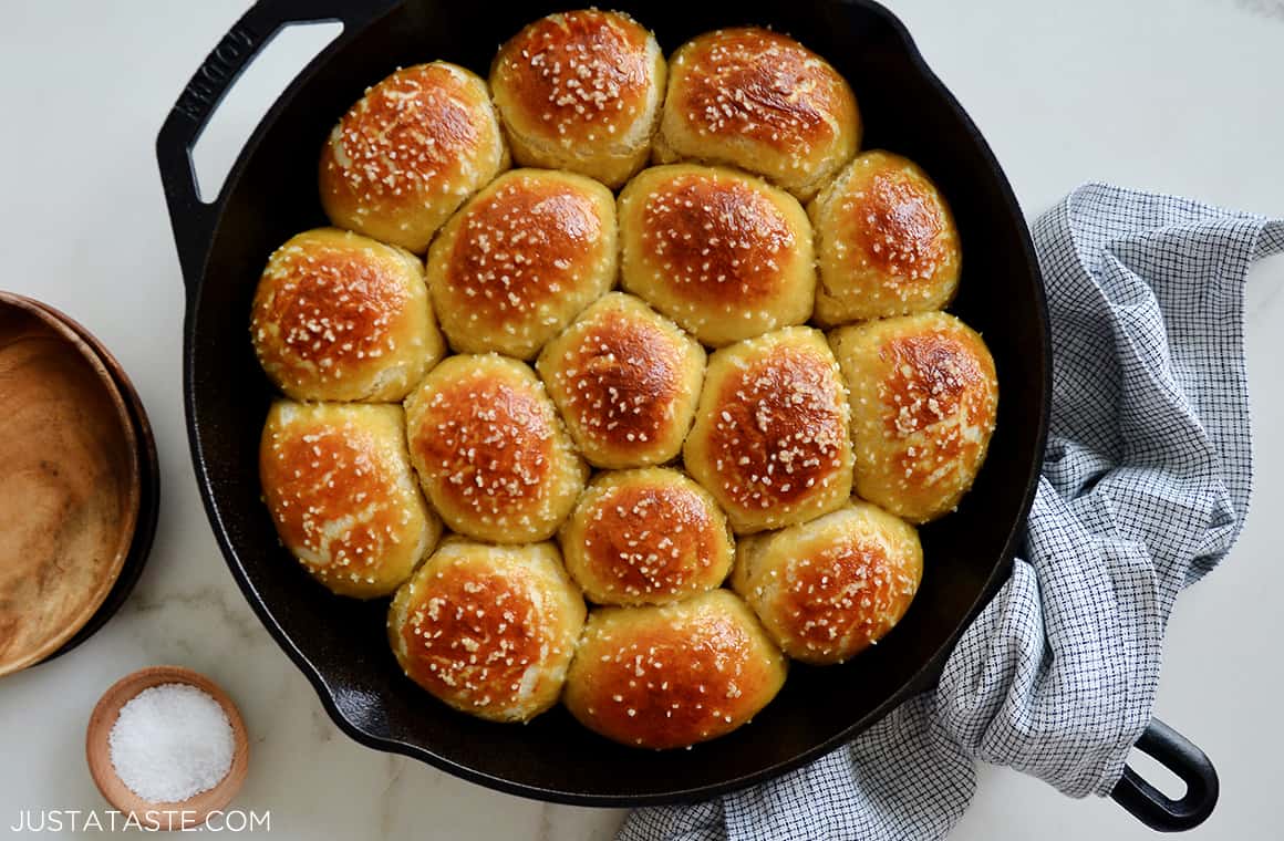 A cast-iron skillet filled with pretzel rolls and a napkin wrapped around the handle