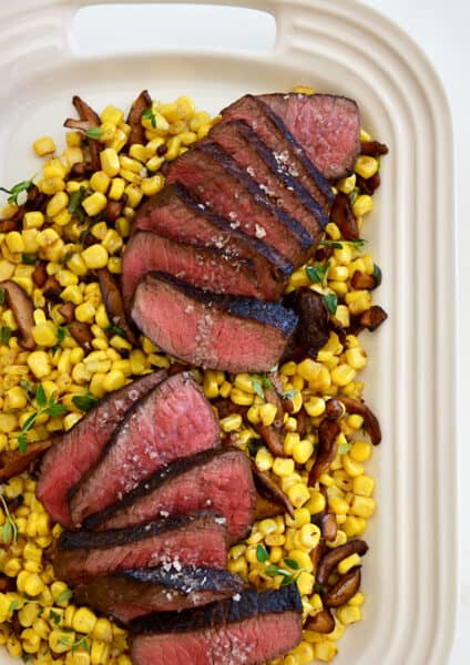 A white platter with corn, mushrooms and sliced steak