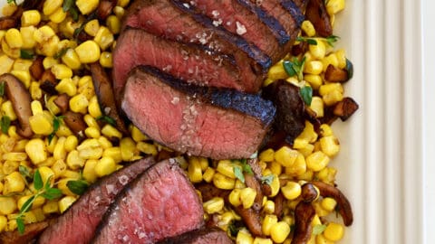 A white platter with corn, mushrooms and sliced steak